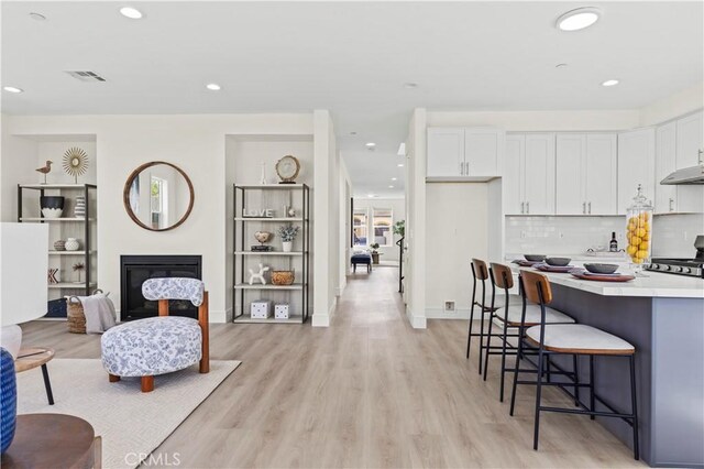 kitchen featuring white cabinetry, a kitchen bar, under cabinet range hood, and range