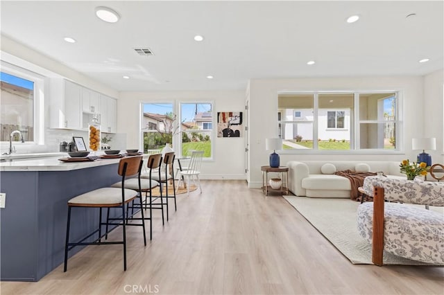 kitchen with a kitchen bar, light wood-style flooring, visible vents, white cabinets, and decorative backsplash