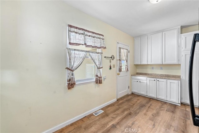 681 E Washington Ave, San Jacinto, CA 92583 - kitchen with baseboards, light wood finished floors, white cabinets, light countertops, and black fridge