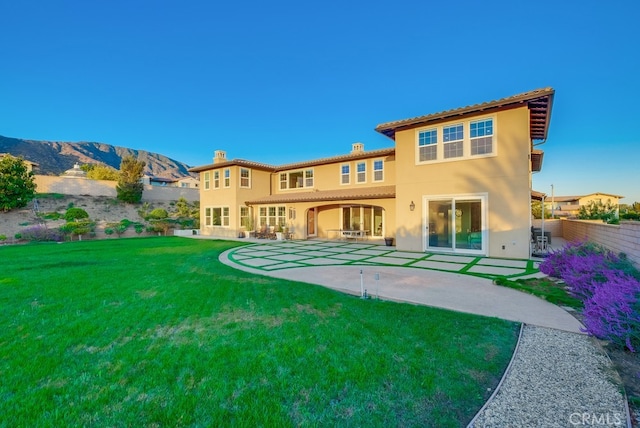 rear view of property with a chimney, fence, stucco siding, a patio, and a lawn