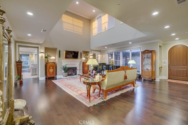 living area with dark wood finished floors, visible vents, a glass covered fireplace, baseboards, and ornamental molding