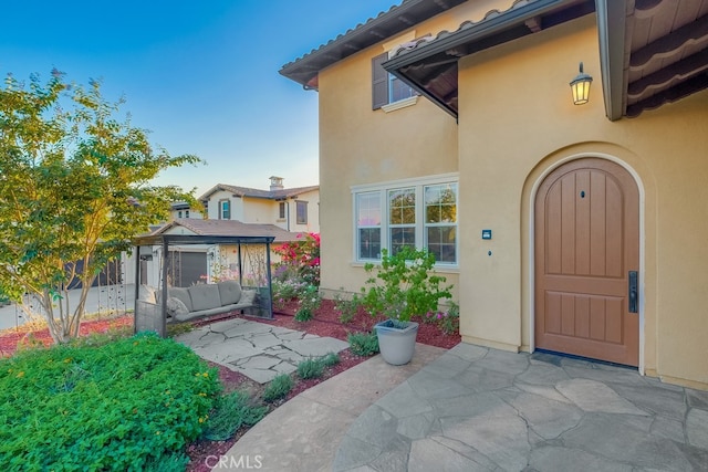 property entrance featuring fence, a tiled roof, stucco siding, a patio area, and an outdoor living space