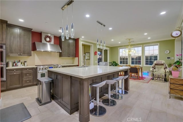 kitchen featuring wall chimney exhaust hood, a sink, a center island with sink, crown molding, and light countertops