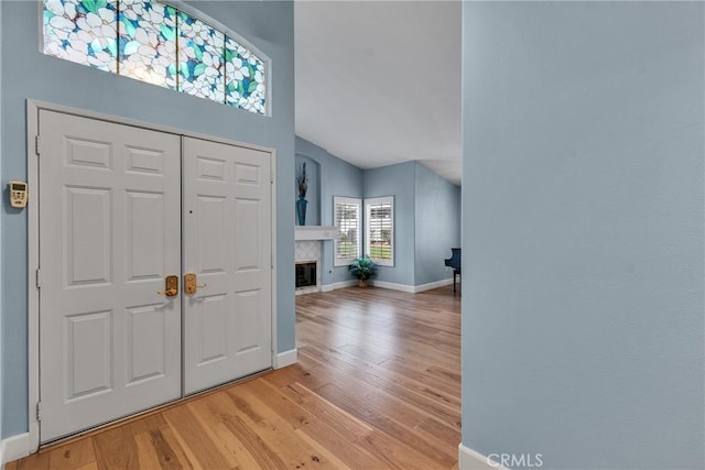 foyer entrance featuring a glass covered fireplace, light wood-type flooring, lofted ceiling, and baseboards