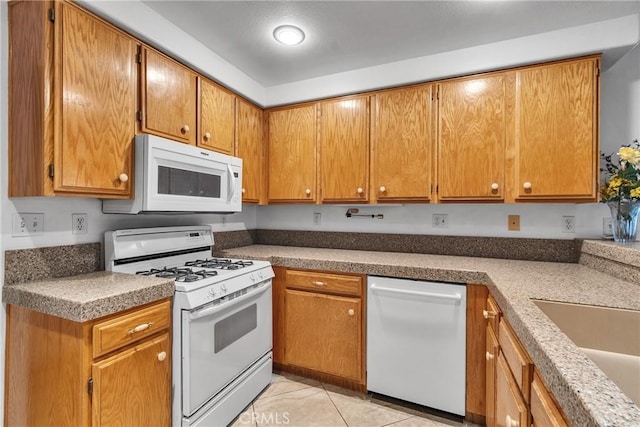 kitchen featuring brown cabinets, light tile patterned floors, a sink, and white appliances