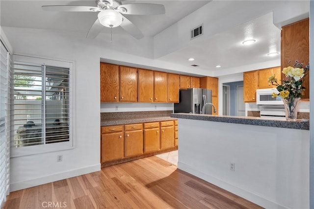 kitchen featuring brown cabinetry, visible vents, white microwave, and stainless steel fridge with ice dispenser