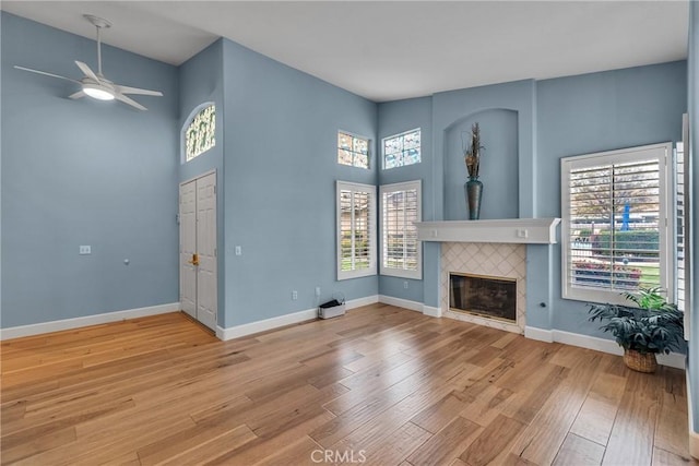 unfurnished living room featuring baseboards, a ceiling fan, a tile fireplace, and light wood-style floors