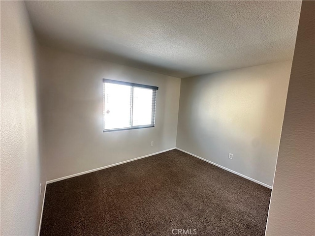 empty room featuring a textured ceiling, dark colored carpet, and baseboards