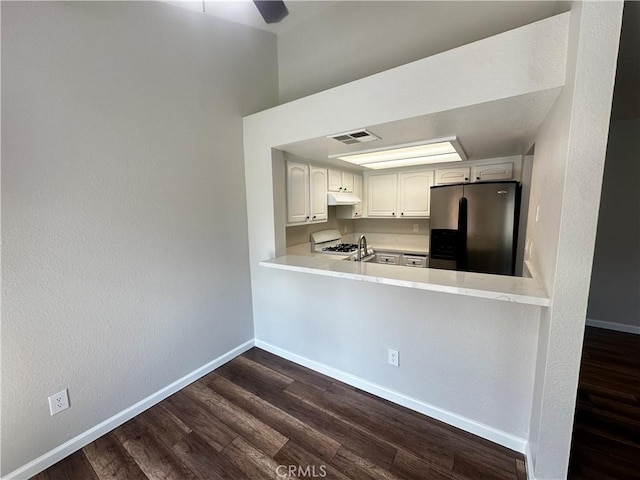 kitchen with white range with gas cooktop, fridge with ice dispenser, under cabinet range hood, light countertops, and dark wood-style floors