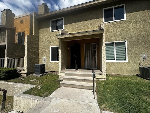 view of exterior entry featuring a yard, a chimney, stucco siding, and central AC