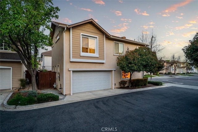 view of front of property with fence, stucco siding, an attached garage, and aphalt driveway