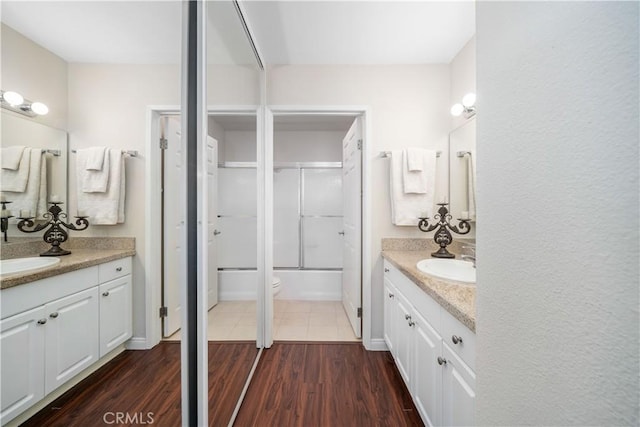 bathroom with a sink, bath / shower combo with glass door, two vanities, and wood finished floors