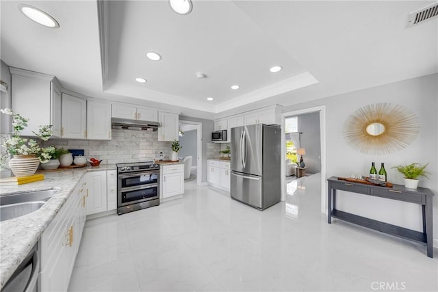 kitchen with under cabinet range hood, visible vents, stainless steel appliances, and a raised ceiling