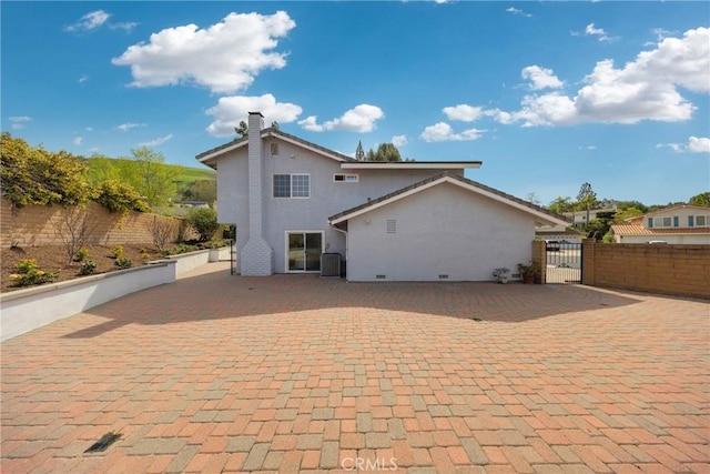 rear view of house with fence private yard, a gate, stucco siding, and a chimney