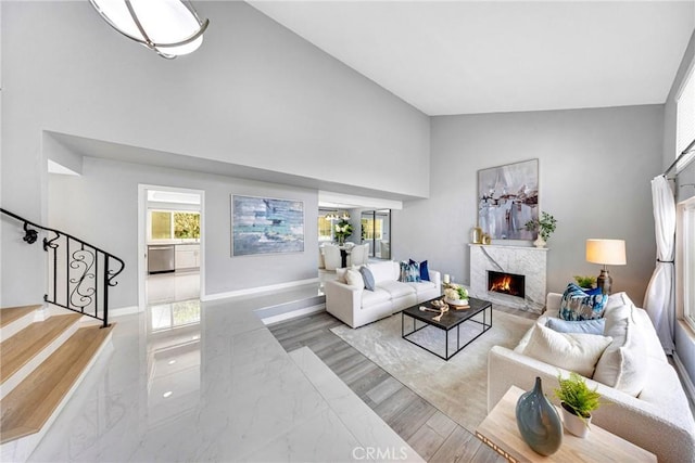 living area featuring baseboards, high vaulted ceiling, a high end fireplace, and stairway