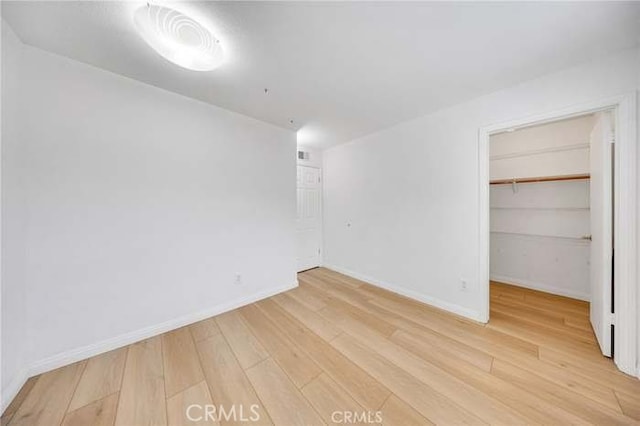 unfurnished bedroom with a closet, baseboards, a spacious closet, and light wood finished floors