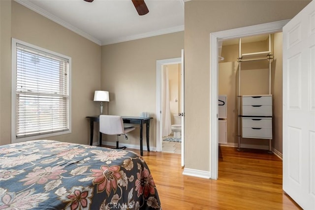 bedroom featuring crown molding, a spacious closet, light wood-type flooring, ensuite bathroom, and baseboards