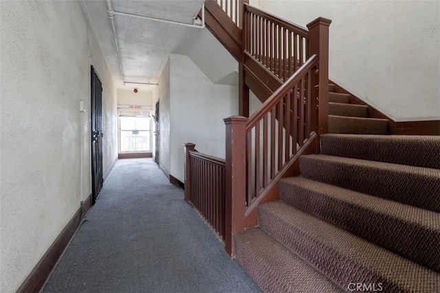 stairs featuring baseboards, a textured wall, carpet, and attic access