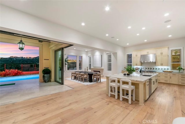 31 Seawatch, Newport Coast, CA 92657 - kitchen featuring under cabinet range hood, light wood-type flooring, a kitchen island with sink, cream cabinets, and tasteful backsplash
