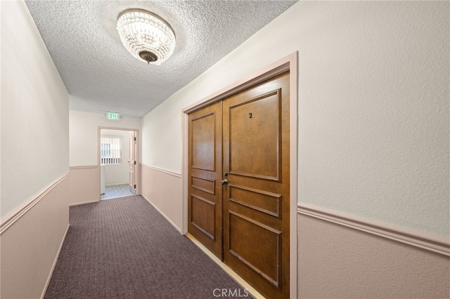 corridor with carpet floors, a textured wall, and a textured ceiling
