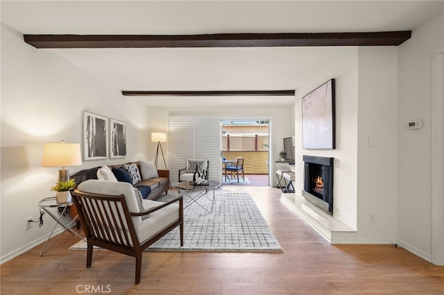 living area with baseboards, beamed ceiling, a lit fireplace, and wood finished floors