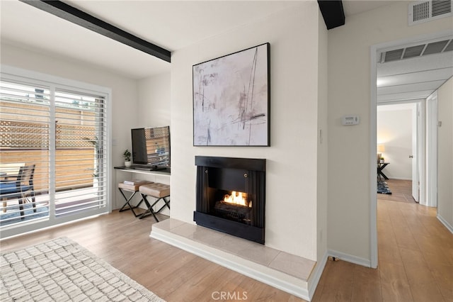 living room with visible vents, beam ceiling, wood finished floors, and a multi sided fireplace