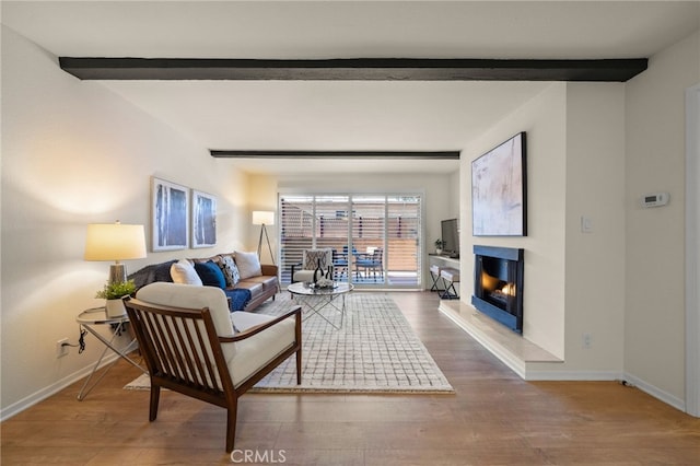 living area with baseboards, beamed ceiling, and wood finished floors