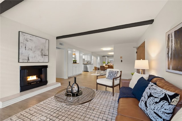 living room featuring a warm lit fireplace, visible vents, wood finished floors, and beam ceiling