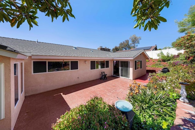 rear view of house featuring stucco siding, roof with shingles, fence, and a patio area