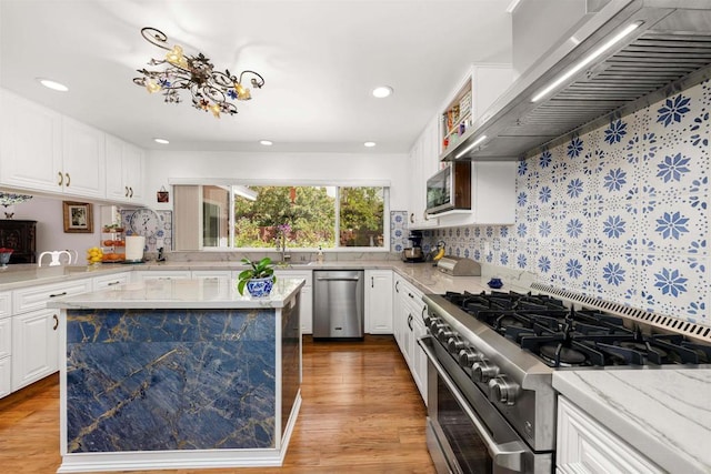 kitchen with wall chimney exhaust hood, stainless steel appliances, backsplash, and white cabinetry