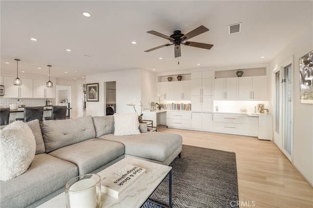 living room with light wood-type flooring, a ceiling fan, visible vents, and recessed lighting