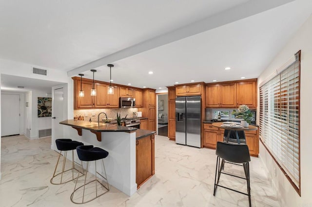 kitchen with brown cabinetry, marble finish floor, stainless steel appliances, a peninsula, and backsplash
