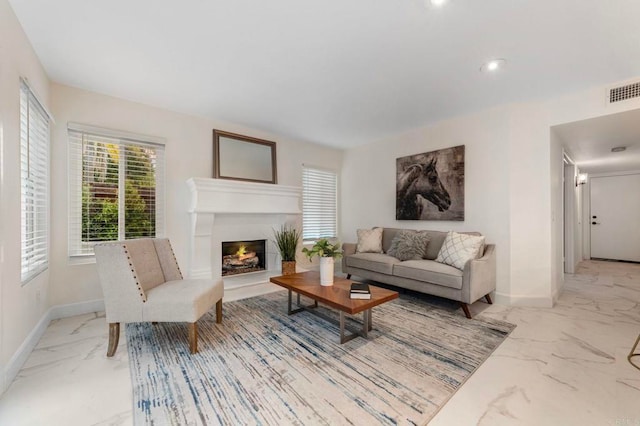 living area featuring baseboards, visible vents, a warm lit fireplace, and marble finish floor