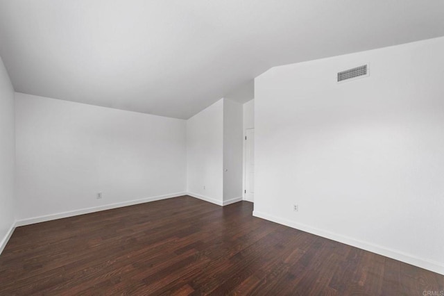 spare room with baseboards, vaulted ceiling, dark wood-type flooring, and visible vents