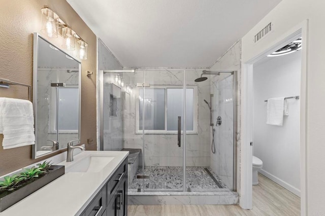 bathroom featuring toilet, visible vents, a marble finish shower, and vanity