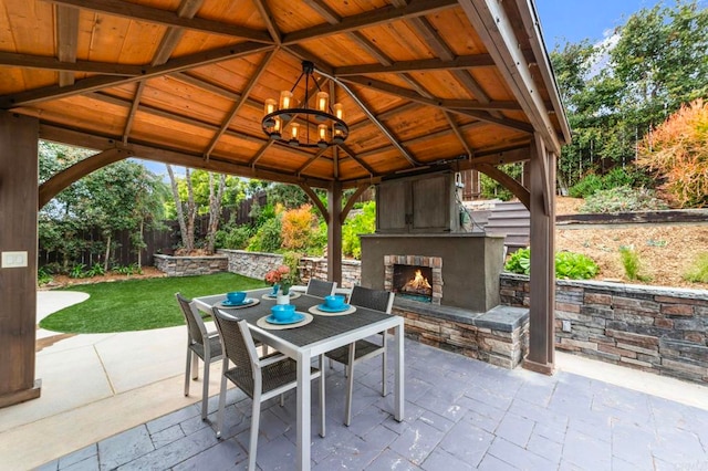 view of patio featuring a gazebo, outdoor dining area, an outdoor stone fireplace, and fence