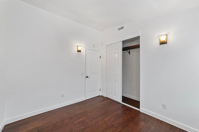 unfurnished bedroom with baseboards, wood finished floors, visible vents, and a closet