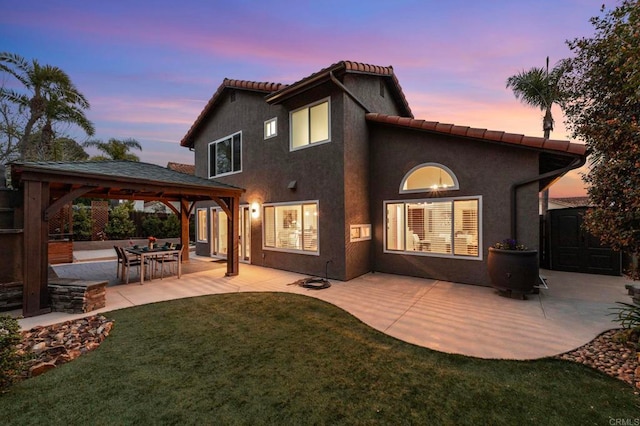 back of house at dusk with a yard, a patio, a gazebo, and stucco siding
