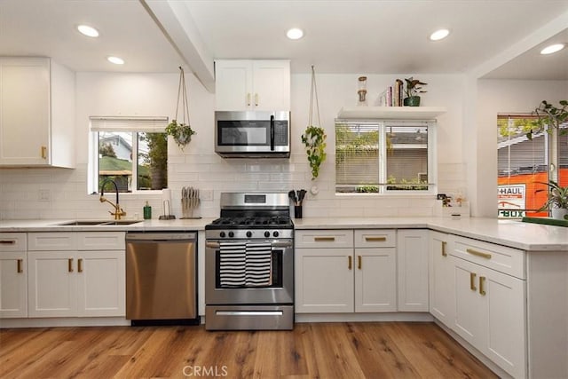 kitchen with white cabinets, appliances with stainless steel finishes, a sink, light countertops, and a peninsula