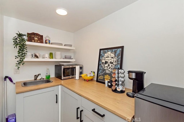 kitchen with open shelves, a sink, light countertops, white cabinets, and stainless steel microwave