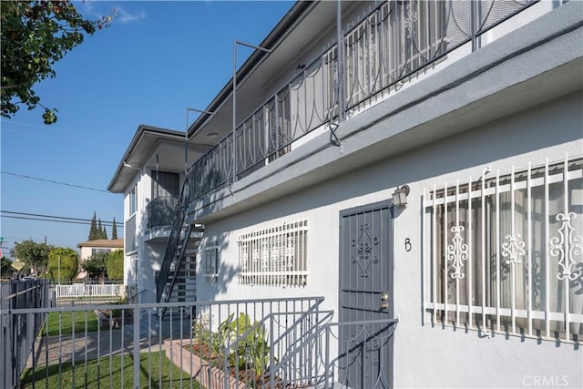 view of side of home with stucco siding, fence, and stairway