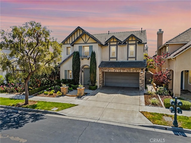 tudor home featuring a tile roof, stone siding, concrete driveway, an attached garage, and stucco siding