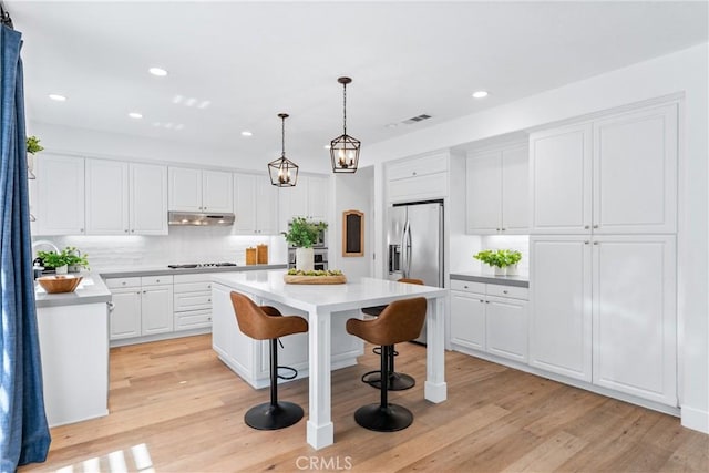kitchen featuring stainless steel appliances, a center island, decorative backsplash, light countertops, and under cabinet range hood