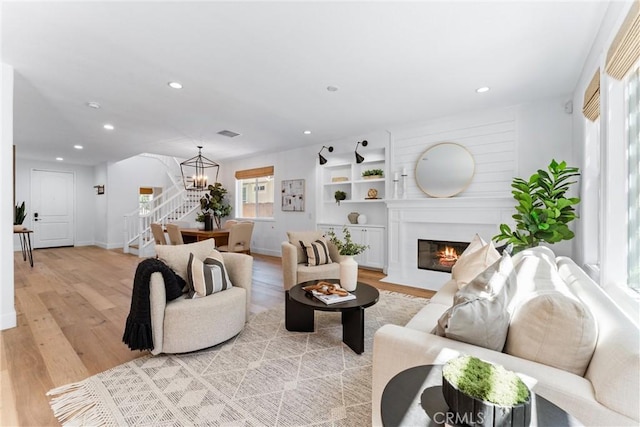 living room featuring stairs, a chandelier, light wood-style floors, a fireplace with flush hearth, and recessed lighting