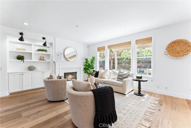 living area featuring baseboards, a lit fireplace, light wood-style floors, and recessed lighting