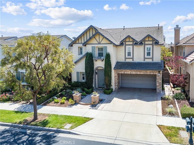 tudor home featuring concrete driveway, a tile roof, stucco siding, and a garage