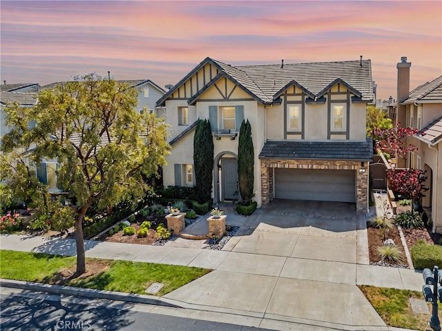 tudor home featuring stucco siding, stone siding, concrete driveway, and a garage