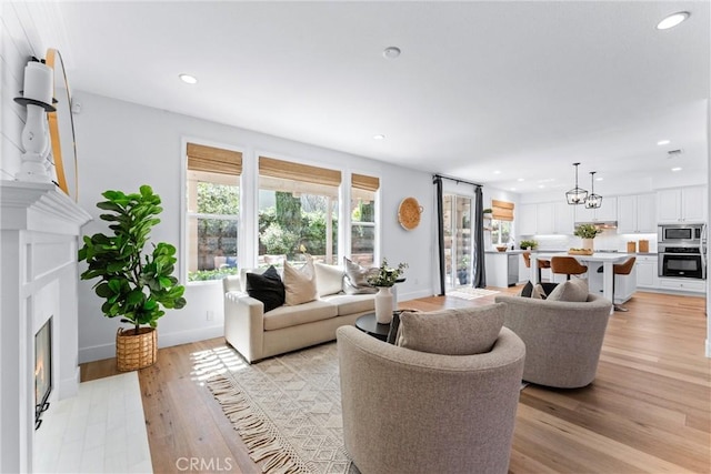living area featuring light wood finished floors, baseboards, a glass covered fireplace, and recessed lighting