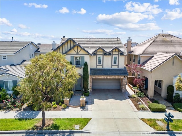 english style home with a tiled roof, a chimney, concrete driveway, an attached garage, and stucco siding