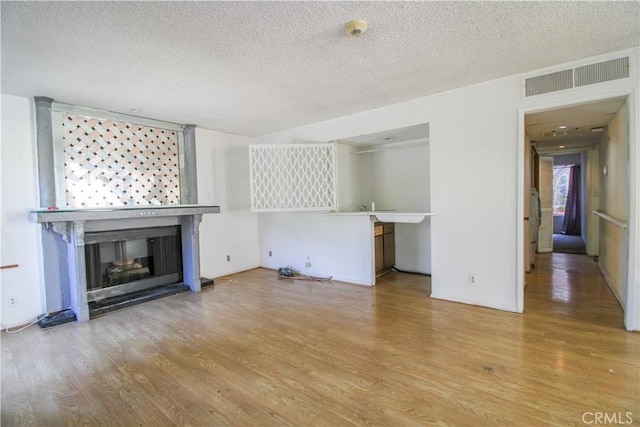 unfurnished living room featuring a multi sided fireplace, a textured ceiling, visible vents, and wood finished floors